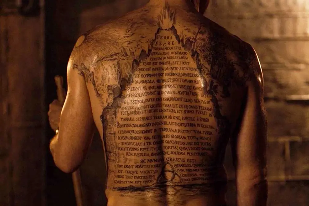 Fotografia de la espalda de un hombre que lleva tatuaje de la tabla esmeralda en la misma